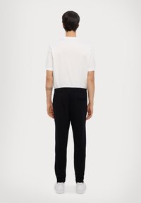Weißes T-Shirt mit kurzen Ärmeln und Rundhalsausschnitt, kombiniert mit schwarzen Jogginghosen mit elastischem Bund und einer Gesäßtasche. Weiße Sneakers.