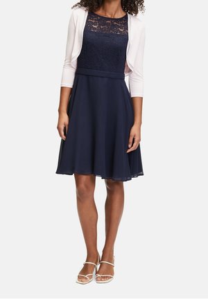 Navy dress with lace bodice and A-line skirt, complemented by a white cropped cardigan. Smooth texture and knee-length design.
