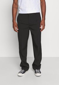 Black tailored trousers with a straight-cut design, featuring a smooth texture, belt loops, and side pockets. Worn with black sneakers.