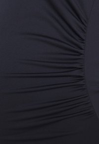 Tecido azul marinho com um brilho subtil, apresentando uma textura franzida ao longo do lado, criando um efeito drapeado. Superfície suave, material elástico.