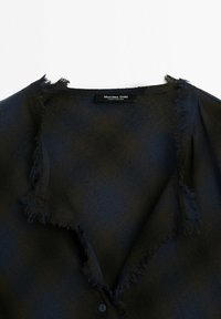 Haut noir texturé avec bords effilochés le long de l'encolure et étiquette « Massimo Dutti Made in Portugal » à l'intérieur du col.