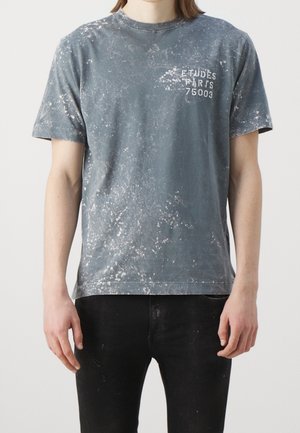 Grijs katoenen T-shirt met een verouderde afwerking, voorzien van spetters en witte bedrukte tekst: "ETUDES PARIS 75003" op de borst.