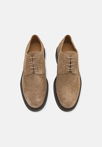 Light brown suede oxford shoes featuring brogue detailing, round toe, and beige laces. Contrasting black sole with stitching accents.
