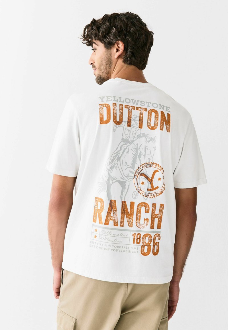 Valge lühikeste varrukatega T-särk, millel on graafiline print "Yellowstone Dutton Ranch" oranžis ja hallis värvitoonis ning hobusõitja illustratsioon.
