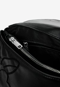 Musta nahkalaukun sisusta, jossa on sileä rakenne, hopeinen vetoketju ja kontrastinvärinen musta vuori. Hienovarainen kohokuvioitu kuvio näkyvissä.