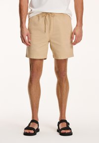Shorts bej dintr-un material ușor, având o talie elastică cu șnur și o croială lejeră, care se termină deasupra genunchiului.