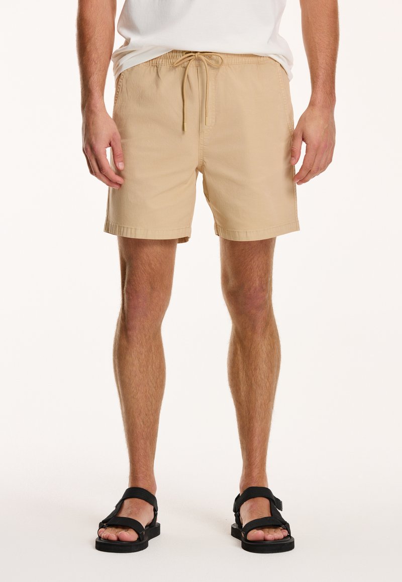 Shorts bej dintr-un material ușor, având o talie elastică cu șnur și o croială lejeră, care se termină deasupra genunchiului.