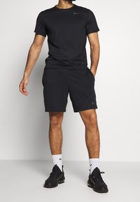 Czarny sportowy T-shirt z krótkimi rękawami, w połączeniu z czarnymi szortami. Zawiera logo Nike w szarym kolorze. Noszony z czarnymi sneakerami i białymi skarpetkami.