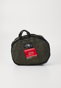 Grønn mesh reiseveske med svarte detaljer, med en rød etikett. Oval form, doble håndtak og glidelås for sikker oppbevaring.