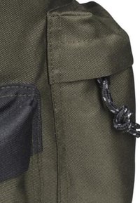 Sac en tissu vert olive avec une surface texturée, doté d'un cordon noir noué et d'une poche latérale avec un panneau noir.