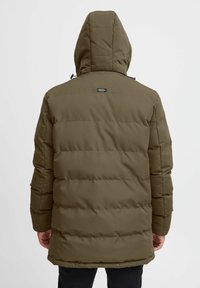 Giacca puffer verde oliva con cappuccio, caratterizzata da un design trapuntato, cuciture frontali e un piccolo logo sulla parte superiore della schiena. Il tessuto esterno appare liscio.