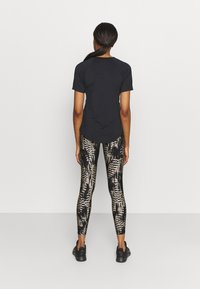 Maglietta nera a maniche corte abbinata a leggings testurizzati e decorati in nero e oro. Il completo include scarpe sportive nere.