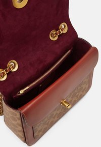 Brązowa skórzana torebka z monogramowym płótnem na zewnątrz. Wnętrze wykończone burgundowym zamszem, ze złotymi okuciami i kieszenią na zamek.