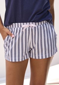 Gestreifte Shorts mit einem weißen Grund und navyblauen vertikalen Streifen, ausgestattet mit einem weichen Bündchen und einer rosa Kordel. Zwei seitliche Taschen sind sichtbar.