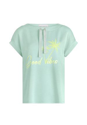 Miętowo-zielona koszulka z krótkim rękawem z podwiniętymi mankietami, srebrnymi sznurkami przy dekolcie, żółtą grafiką palmy i napisem „Good Vibes” na przodzie.