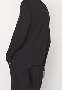 Felpa nera realizzata in morbido tessuto, caratterizzata da un design semplice, polsini e orlo a coste, con una vestibilità comoda e tasche laterali.