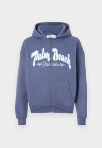 Marineblå lynlås hoodie lavet af bomuld med en blød tekstur. Har en hætte med snøre og et stort "Palm Beach Florida" grafisk tryk.