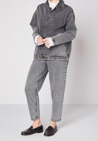 Dunkelgraue Jeansjacke mit Knopfschluss und oversized Passform. Kombiniert mit passenden grauen, schmal zulaufenden Jeans und schwarzen Slippern.