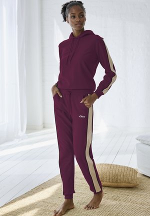 Himbeerfarbener Hoodie mit Kordelzug und cremefarbenen Seitenstreifen, kombiniert mit passenden himbeerfarbenen Jogginghosen mit cremefarbenen Akzenten und Taschen.
