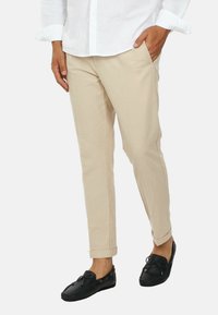 Pantaloni beige su misura con una trama liscia, vestibilità affusolata e orli arrotolati, abbinati a mocassini neri con dettaglio a fiocco.