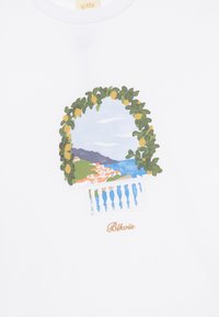 T-shirt blanche ornée d'un graphique coloré d'un balcon avec vue côtière, encadré par des feuilles vertes et des citrons. Nom de la marque "Bleviis" en doré.