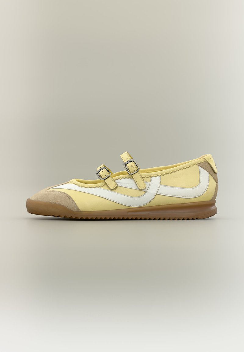 Chaussure Mary Jane jaune avec deux brides à boucle, détail Swoosh latéral blanc, bout beige et semelle marron rainurée.