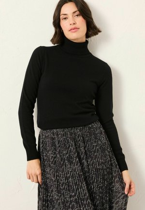 Schwarzer, figurbetonter Rollkragenpullover aus weichem Material, kombiniert mit einem schwarzen Plisseerock mit einem weißen abstrakten Muster.