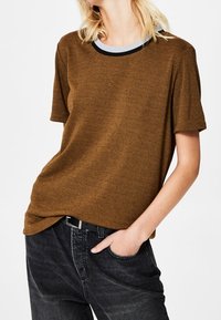 Brun T-shirt med korte ærmer og rund halsudskæring med kontrast i grå og sort. Blød tekstur, let løs pasform, kombineret med sorte jeans.