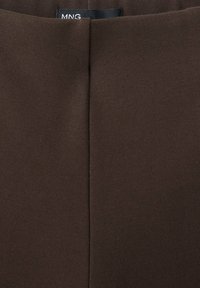 Vêtement en tissu brun foncé avec une couture centrale et une petite étiquette noire de la marque MNG en haut du bord.