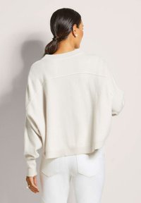 Witte, cropped trui met een losse fit, geribbelde manchetten en een wijde halslijn. Zachte textuur en brede mouwen, gecombineerd met aansluitende witte broeken.