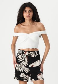 Biely crop top s odhalenými ramenami a zúženými okrajmi, skombinovaný s čiernymi šortkami s bielym a červeným tropickým vzorom listov a opaskom v páse.