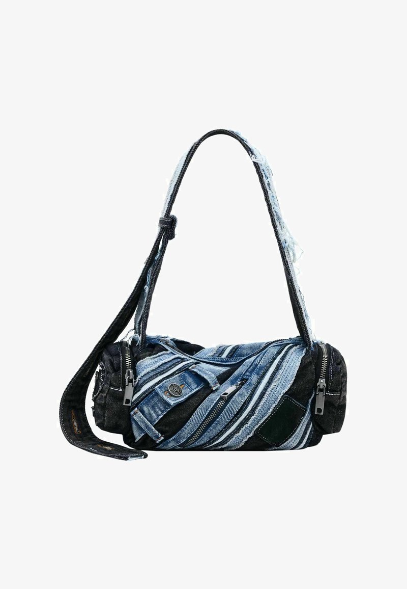 Bolsa de mezclilla con forma cilíndrica, que combina telas azules y negras, múltiples cremalleras y bordes deshilachados para darle textura.
