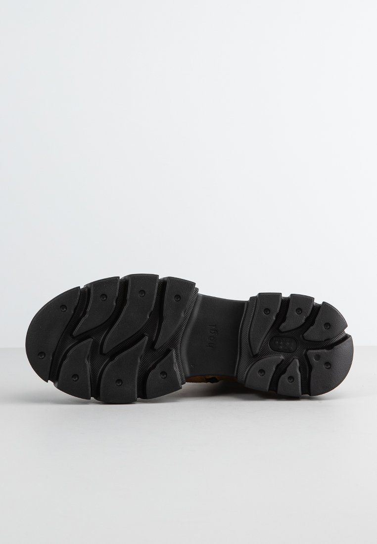 Suela de zapato de goma negra con un patrón texturizado, que presenta surcos profundos y ranuras distintivas para proporcionar tracción. Forma plana y ancha para ofrecer estabilidad.