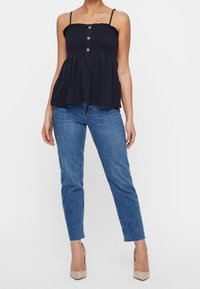 Marineblaues Peplum-Top mit dünnen Trägern und drei vorderen Knöpfen, kombiniert mit hellblauen Slim-Fit-Jeans und beigen High Heels.