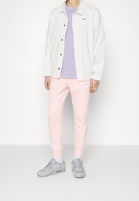 Bílá košile na knoflíky přezdívající k levandulovému tričku, doplněná o světle růžové tepláky a šedé sportovní boty. Obsahuje akcenty s logem značky.