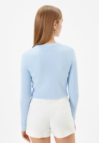 Ljusblå ribbad tröja med långa ärmar och rund hals, cropped design, kombinerad med vita shorts, synlig detalj på ryggen.