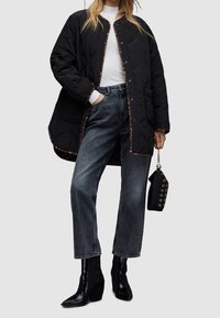 Czarna pikowana kurtka z kontrastowymi wykończeniami w zwierzęcy wzór, zestawiona z wysokim stanem wyblakłych jeansów i czarnymi botkami na obcasie. Mała czarna torebka.