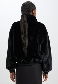 Černá bunda z umělé kožešiny s vysokým límcem, volným střihem, žebrovanými manžetami a lemem, hladkou texturou a bez viditelných zapínání.