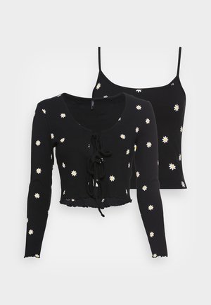 Crop top court en tissu côtelé noir avec manches longues et liens à l'avant, assorti à un débardeur à fines bretelles, tous deux ornés de motifs de marguerites blanches.