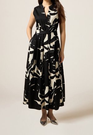 Mouwloze zwart-witte midi-jurk met abstract patroon, V-hals en getailleerde taille, gecombineerd met zilverkleurige pumps met puntige neus.