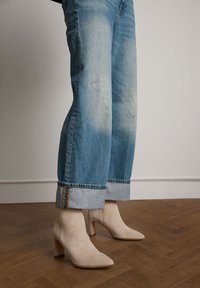 Beige suède enkellaarsjes met een puntige neus en een blokhak, gecombineerd met lichtblauwe opgerolde spijkerbroeken met een geel-blauw gestreepte zoom.