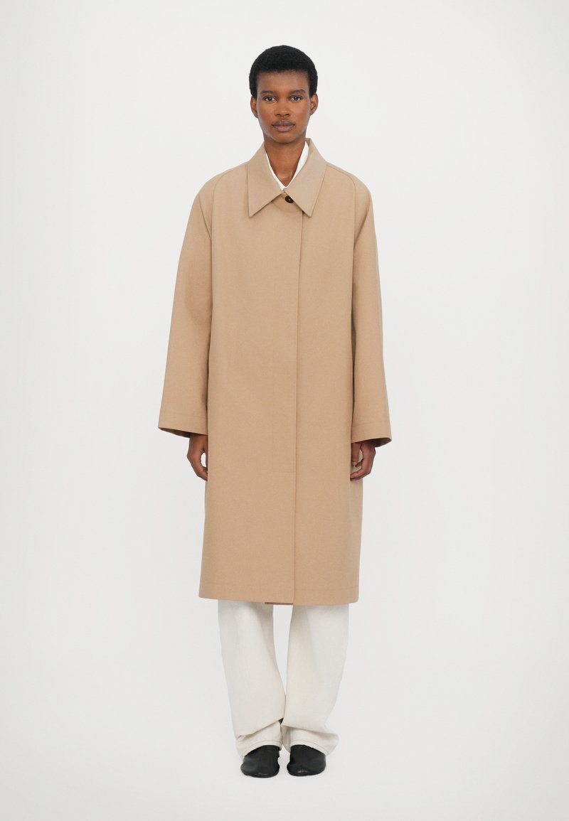 Beige, long coat with a wide collar, made of a smooth fabric. Features a single button closure and relaxed, oversized sleeves.