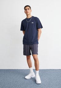 Mørkeblå bomulds t-shirt med et lille grafisk logo, parret med ternede shorts i mørkeblå, rød og hvid. Afsluttet med hvide sneakers og sokker.