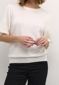 Top de punto color crema con mangas cortas acanaladas, escote redondo y corte relajado. Combinado con pantalones negros que presentan una textura suave.