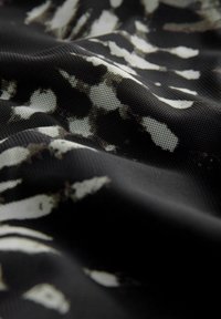 Zwarte stof met een wit en grijs abstract patroon, met een gladde textuur en een lichte glans, gevouwen om diepte en detail te tonen.