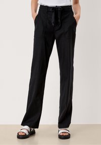 Pantalons noirs à jambes larges en tissu léger, dotés d'une taille à cordon de serrage et de deux poches avant, présentés avec des sandales.