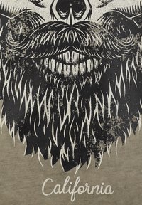 Camiseta gráfica con una ilustración en blanco y negro de una barba y un bigote, con la palabra "California" impresa en texto blanco debajo.