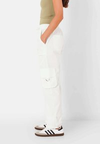 Witte cargobroek met zijzakken, met een verstelbare tailleband. Draag met zwart-witte sneakers en een aansluitend olijfgroene top.