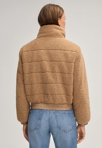Brązowa, fakturowana polarowa kurtka z wysokim kołnierzem, żeberkowym wykończeniem u dołu i mankietami. Posiada pikowany wzór na plecach i luźny krój.