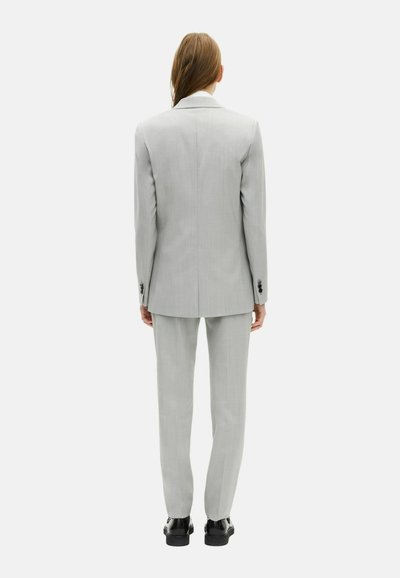 Completo tailored grigio chiaro con giacca a un bottone, pantaloni slim fit e scarpe nere, che mostrano una texture liscia e un design strutturato.